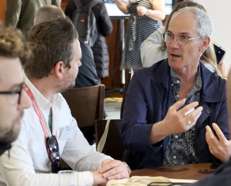 Two men in conversation whilst sat at a table.